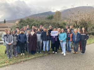Au premier plan les participants de la réunion Natur'Adapt sont réunis. L'une d'entre eux porte une pancarte où il est écrit "Natur'Adapt"