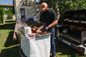Le prestataire découpe sa viande de porc, tandis qu'un cochon grille en arrière plan.