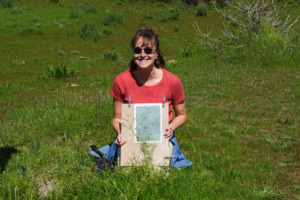 Une jeune femme pause au milieu de l'herbe, exposant fièrement son cyanotype dans ses mains